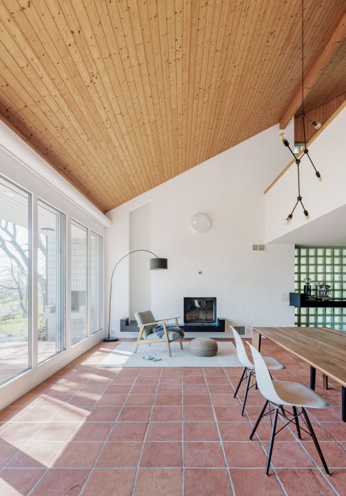 ein überhoher Raum mit einer Holzdecke und Bodenplatten aus Ton, ein Kamin und Stühle an einem Esstisch