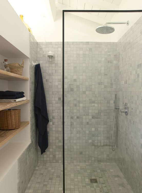 Eine moderne Dusche mit einer schwarz umrahmten Duschwand aus Glas, rustikalen Marmorfliessen und einem linkerhand in die Wand eingebauten Wandregal mit Holztablaren.