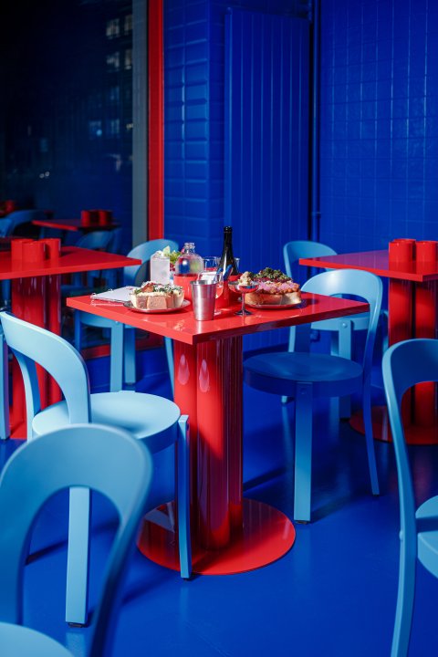 Ein roter Tisch, blaue Stühle in einem blauen Raum. Auf den Tisch stehen Essen und Getränke.